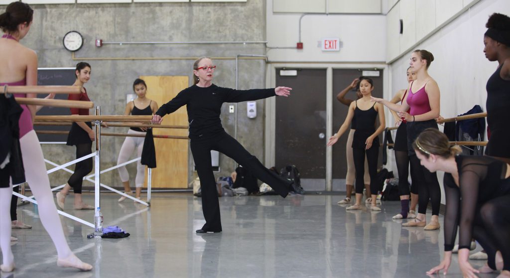 Dance professor Molly Lynch demonstrating with ballet barre, student surrounded